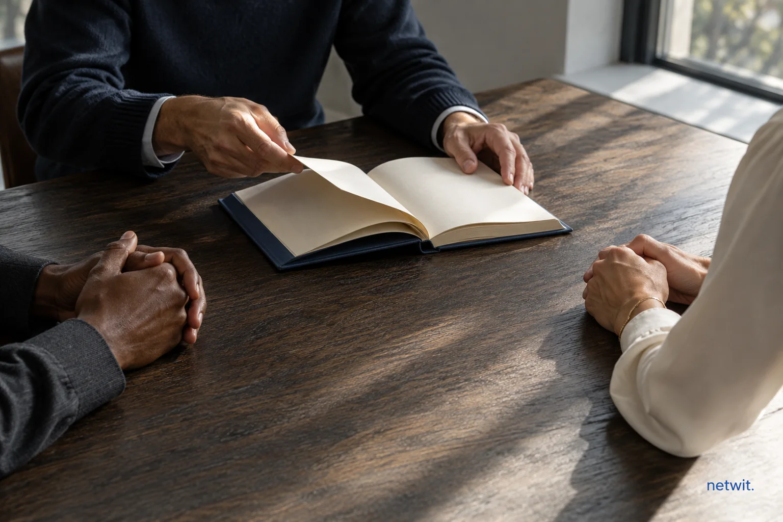 People gathered around an open book at a wooden table.